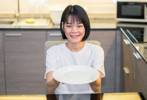 Una donna asiatica che tiene un piatto bianco vuoto nella cucina domestica