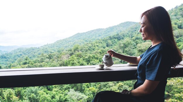 Una donna asiatica che versa il tè in una tazza bianca sulla tavola di legno con la bella vista sulle montagne