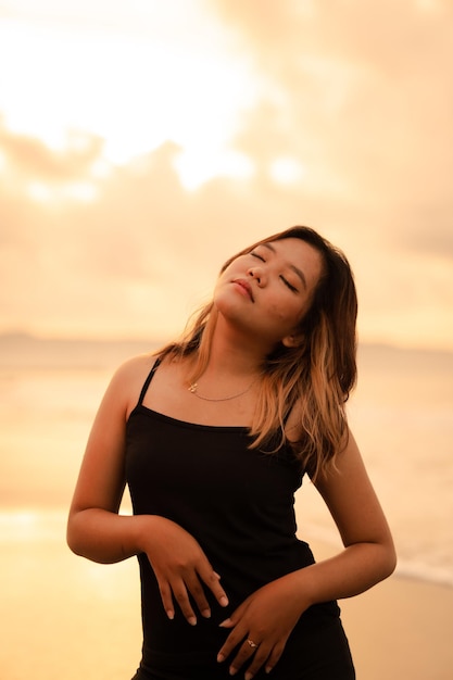 Una donna asiatica con capelli castani e vestiti neri fa pose sexy molto abilmente mentre si gode la spiaggia