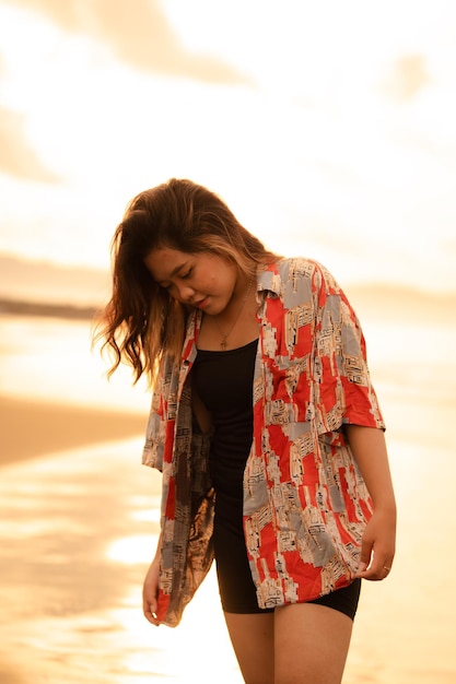 Una donna asiatica con i capelli biondi e una camicia rossa cammina lungo la spiaggia per godersi la vista del mare