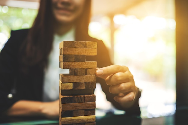 Una donna asiatica costruisce blocchi di legno della torre Tumble per la gestione e la strategia nei concetti di business