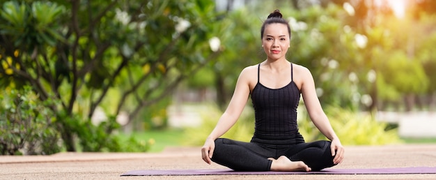 Una donna asiatica di mezza età fiduciosa in abbigliamento sportivo che fa esercizi di yoga sul tappetino da yoga all'aperto in