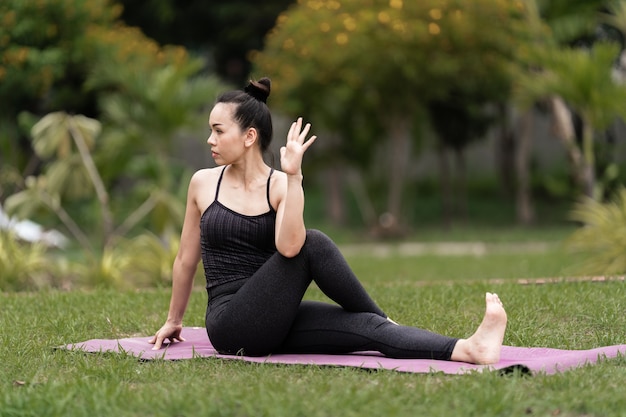 Una donna asiatica di mezza età fiduciosa in abbigliamento sportivo che fa esercizi di yoga sul tappetino da yoga all'aperto in