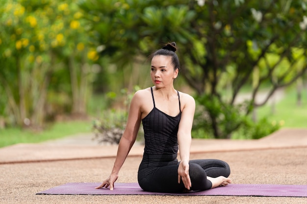 Una donna asiatica di mezza età sicura in abbigliamento sportivo che fa esercizio di yoga sul tappetino da yoga all'aperto nel cortile di casa al mattino. Giovane donna che fa esercizio di yoga all'aperto nel parco pubblico naturale