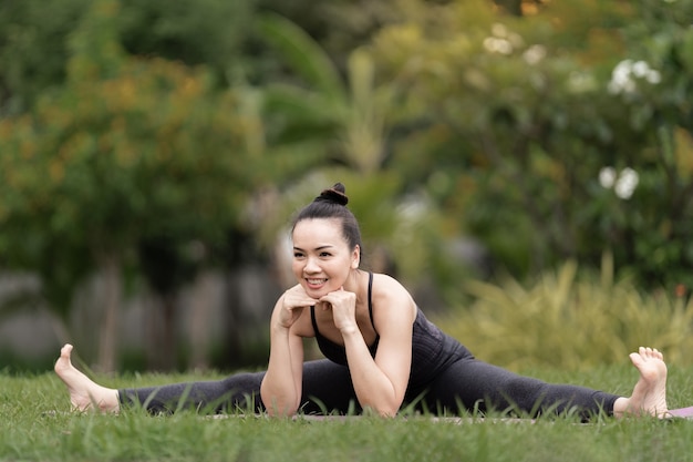 Una donna asiatica di mezza età sicura in abbigliamento sportivo che fa esercizio di yoga sul tappetino da yoga all'aperto nel cortile di casa al mattino. Giovane donna che fa esercizio di yoga all'aperto nel parco pubblico naturale