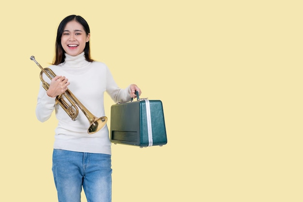 Una donna asiatica di talento sta tenendo la tromba mentre si trova su uno sfondo giallo isolato
