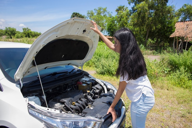 Una donna asiatica ha bisogno di aiuto con un'auto rotta con il cofano aperto