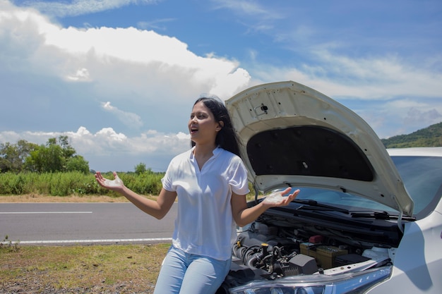 Una donna asiatica ha bisogno di aiuto con un'auto rotta con il cofano aperto