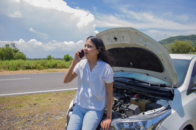 Una donna asiatica ha bisogno di aiuto con un'auto rotta con il cofano aperto