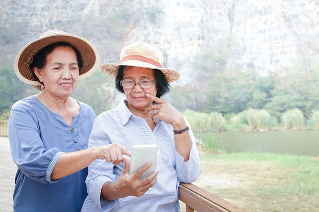 Una donna asiatica senior detiene uno smartphone, scatta foto e riproduce i social media. Le piace andare in pensione. Concetto di comunità anziana. Copia spazio