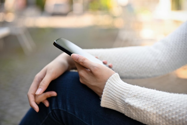 Una donna asiatica si siede nel cortile usando l'immagine della vista laterale dello smartphone