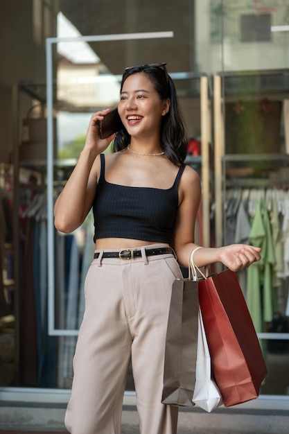 Una donna asiatica sicura di sé sta parlando al telefono con la sua amica durante la sua giornata di shopping in città