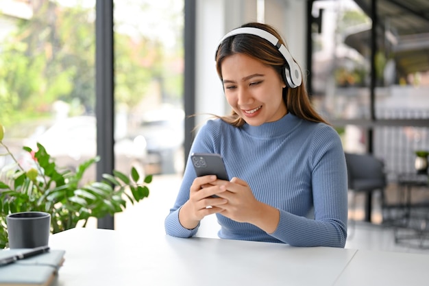 Una donna asiatica sorridente che usa il telefono a un tavolo ama chiacchierare e ascoltare musica