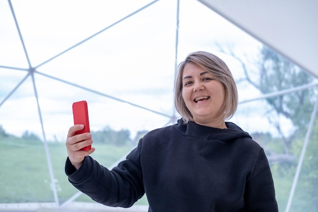 Una donna asiatica sorridente con una giacca nera utilizza uno smartphone per la comunicazione video online agitando la mano