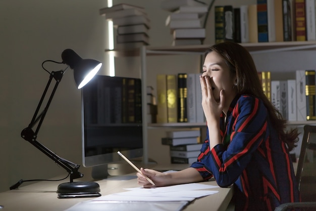 Una donna asiatica sta lavorando duramente, sembra così provata a sbadigliare dato che ha molti lavori