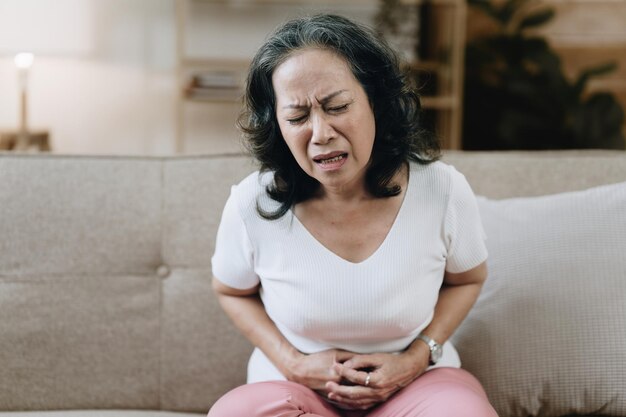 Una donna asiatica sulla ottantina esausta e sotto stress è a casa con mal di stomaco