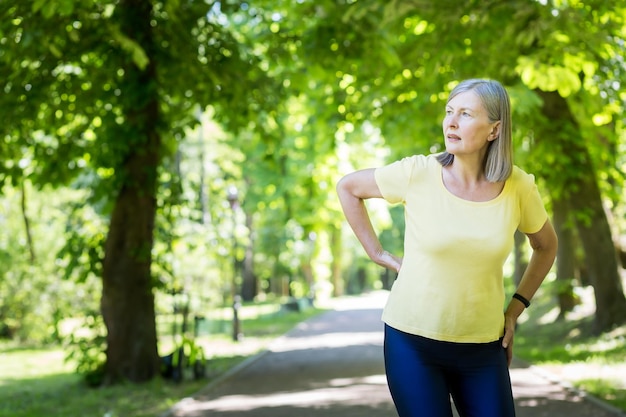 Una donna attiva anziana durante una passeggiata nel parco ha ferito il suo pensionato alla schiena durante una corsa in una giornata estiva