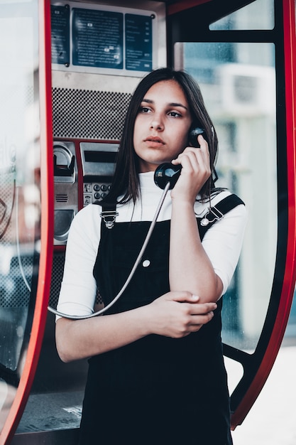 Una donna attraente che fa una telefonata pubblica da una cabina telefonica