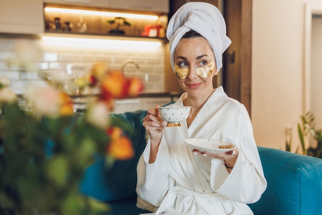 Una donna attraente con la cura della pelle sotto le bende sugli occhi che si gode il caffè del mattino e si rilassa a casa sua.