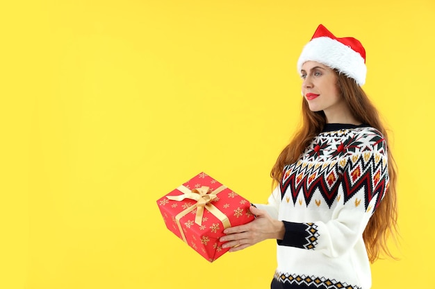 Una donna attraente con un cappello da Babbo Natale tiene una confezione regalo su sfondo giallo