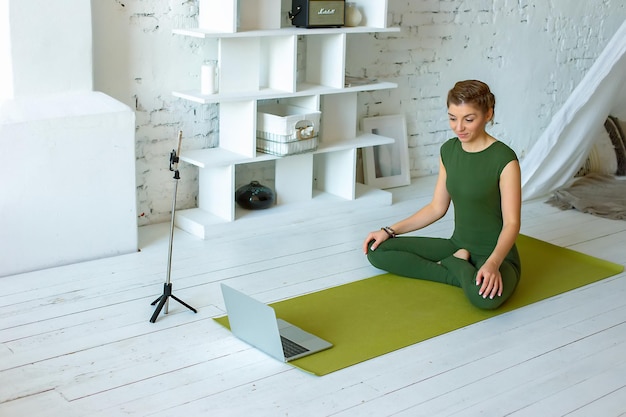 Una donna bella e magra in abiti sportivi verdi scrive lezioni di yoga a casa