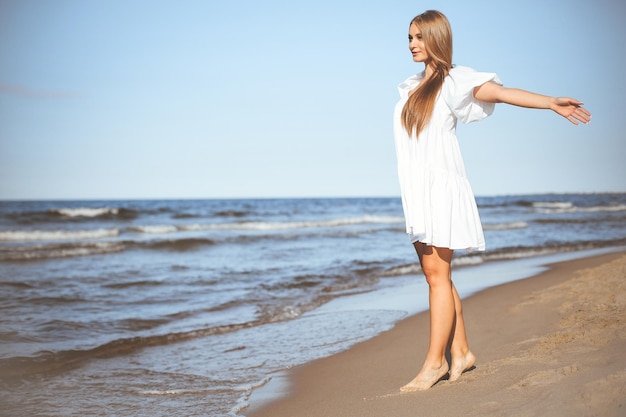 Una donna bella e sorridente sta camminando sulla spiaggia dell'oceano con le braccia aperte.