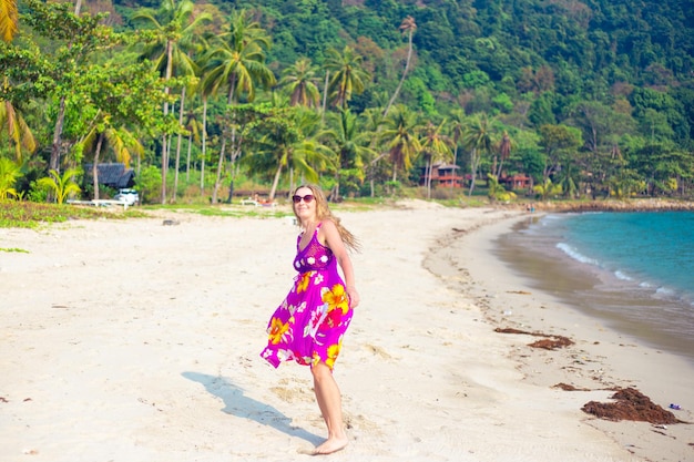 Una donna bionda adulta in un vestito luminoso su una spiaggia tropicale sorride Viaggi e turismo