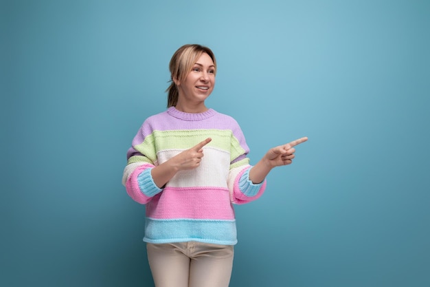 Una donna bionda carina e ordinata in un look casual mostra le mani al muro con lo spazio della copia su un blu