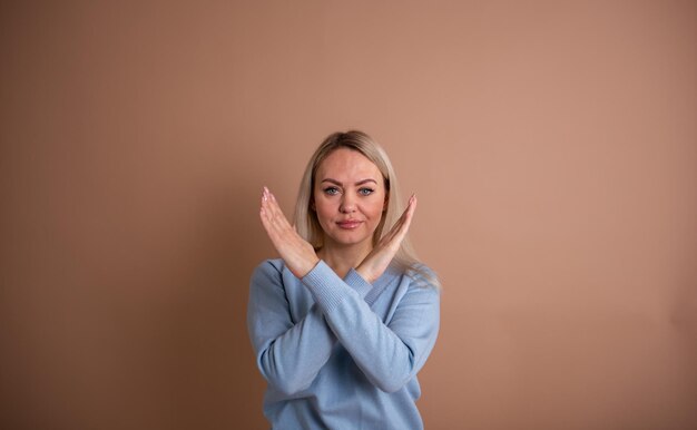 Una donna bionda con un maglione blu mostra con le mani una sosta su uno sfondo beige con un posto per il testo