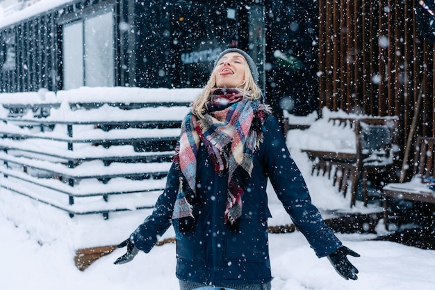 Una donna bionda in piedi sotto una nevicata cattura i fiocchi di neve con la lingua come un bambino che si diverte