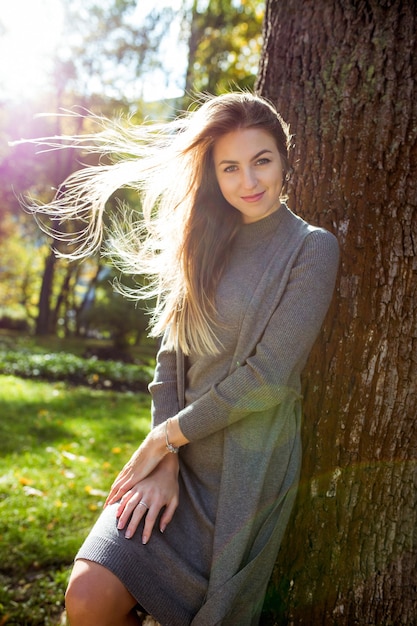 Una donna bionda romantica indossa un abito grigio, con i capelli al vento che posano sotto i raggi del sole