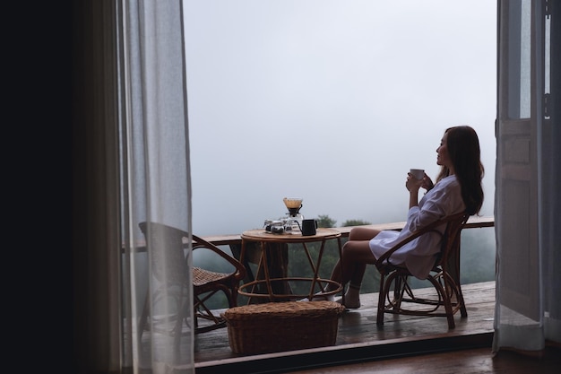 Una donna che beve caffè a goccia con una splendida vista sulla natura in una giornata nebbiosa