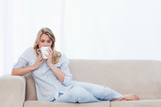 Una donna che beve una tazza di caffè è sdraiata su un divano