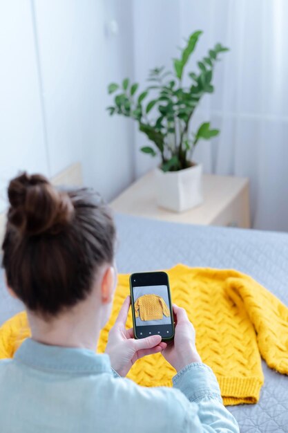 Una donna che carica una foto sul cellulare dei propri vestiti per la vendita online a casa