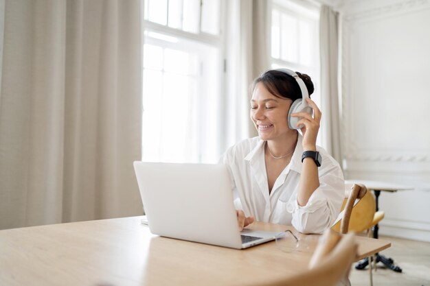 Una donna che indossa le cuffie utilizza un'applicazione per la musica in un computer sul tavolo Si siede