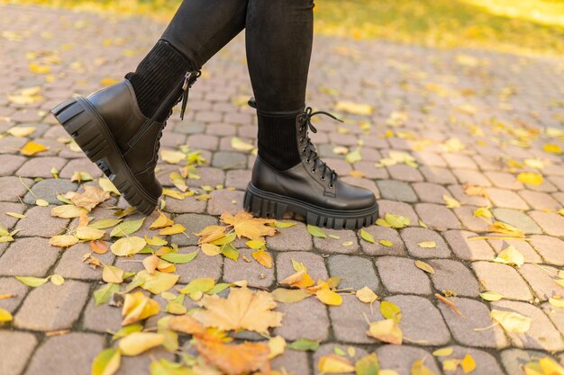 Una donna che indossa stivali neri si trova su un sentiero di mattoni in foglie d'autunno.