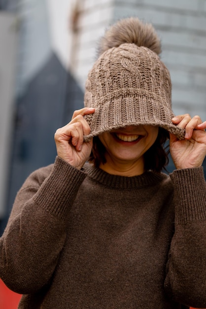 Una donna che indossa un maglione marrone e un maglione marrone tiene il viso rivolto verso il viso e sorride.