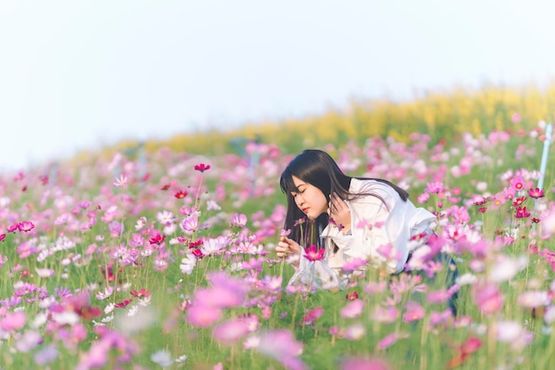 Una donna che indossa una camicia bianca sta annusando i fiori che sbocciano nel giardino del cosmo