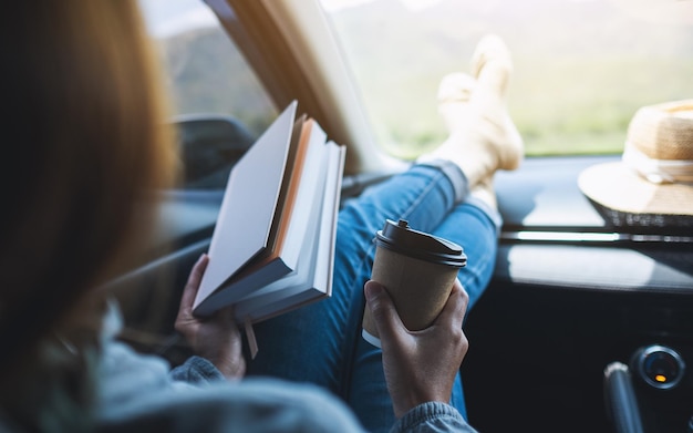 Una donna che legge un libro e beve caffè in macchina