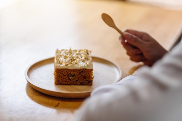 Una donna che mangia un pezzo di torta di carote fatta in casa in un vassoio di legno con un cucchiaio