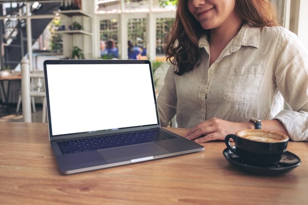 Una donna che presenta il lavoro con il computer portatile mockup con schermo bianco vuoto sul tavolo di legno