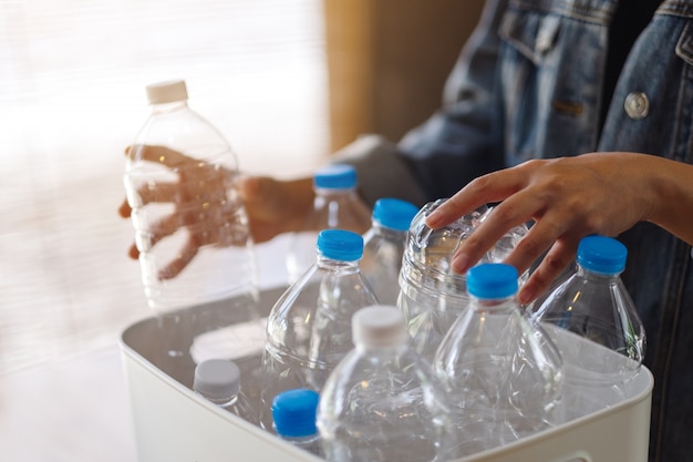 Una donna che raccoglie e separa le bottiglie di plastica riciclabili dell'immondizia in un bidone della spazzatura a casa