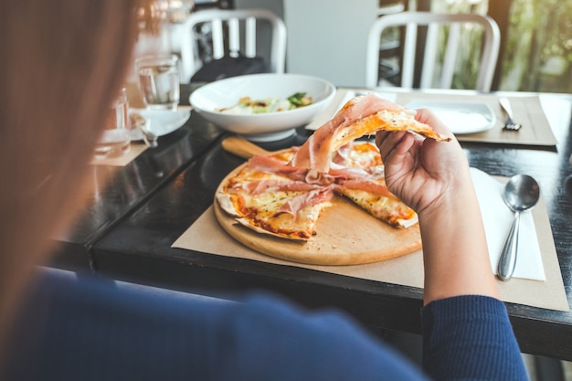 una donna che raccoglie un pezzo di pizza al prosciutto di Parma da mangiare nel ristorante