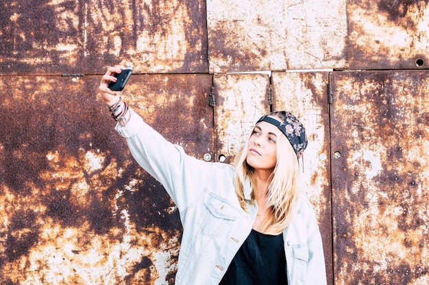 Una donna che scatta una foto di se stessa per strada - una ragazza bionda che si fa un selfie con uno sfondo urbano