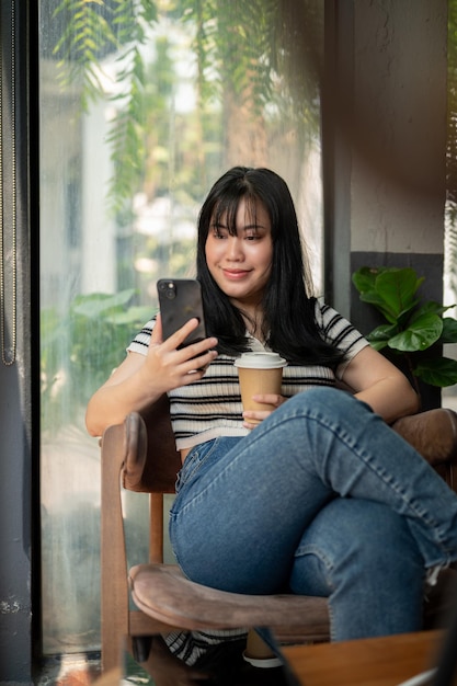 Una donna che si rilassa in un caffè usando il suo smartphone e si gode il suo caffè a un tavolo vicino alla finestra