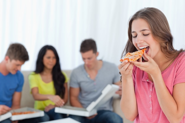 Una donna che sta per mangiare una fetta di pizza con le sue amiche dietro di lei