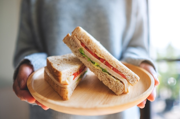 Una donna che tiene due pezzi di panino integrale in un piatto di legno