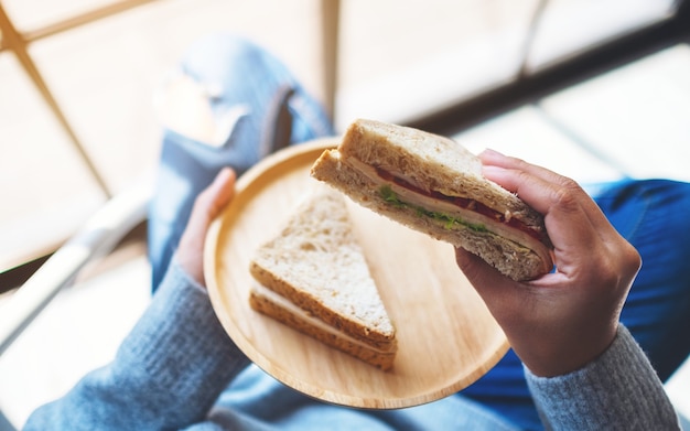 Una donna che tiene e mangia due pezzi di panino integrale in un piatto di legno