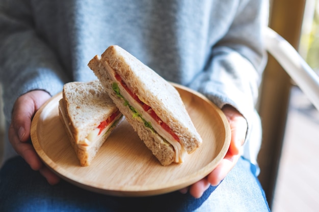 Una donna che tiene e serve due pezzi di panino integrale in un piatto di legno