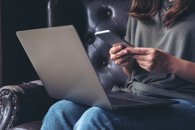 Una donna che tiene e utilizza un telefono cellulare mentre si lavora al computer portatile